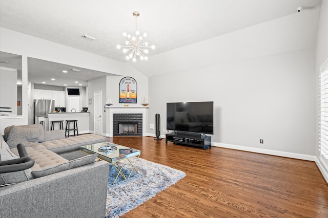 living room featuring wood-type flooring, vaulted ceiling, a brick fireplace, and a notable chandelier