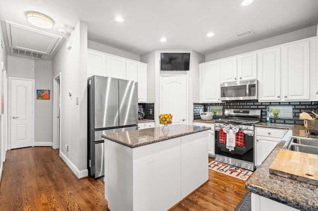 kitchen with appliances with stainless steel finishes, dark stone counters, a center island, dark hardwood / wood-style floors, and white cabinetry