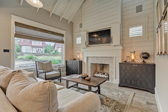 living room with beam ceiling, a tiled fireplace, light hardwood / wood-style flooring, and high vaulted ceiling