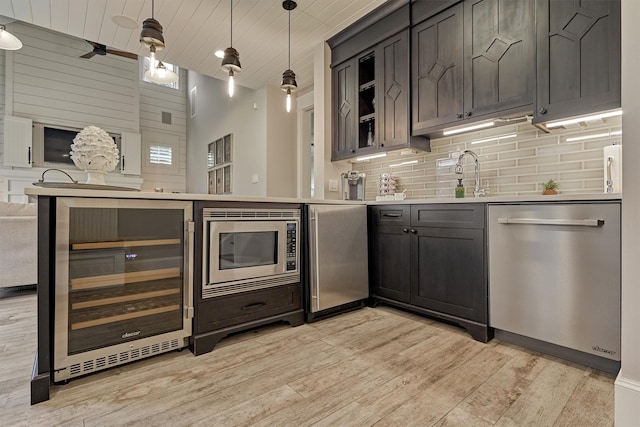 kitchen featuring sink, beverage cooler, stainless steel appliances, decorative light fixtures, and light wood-type flooring