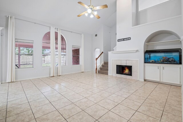 unfurnished living room featuring a tiled fireplace, ceiling fan, light tile patterned flooring, and high vaulted ceiling