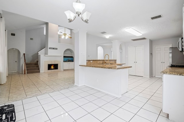 kitchen with sink, light tile patterned floors, decorative light fixtures, light stone counters, and kitchen peninsula