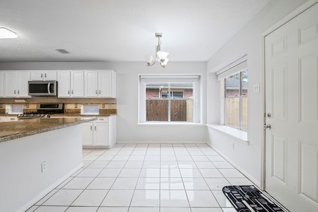 kitchen with dark stone counters, stainless steel appliances, a chandelier, white cabinetry, and hanging light fixtures