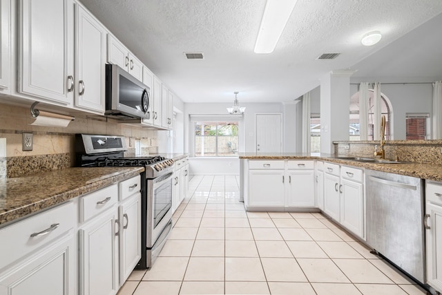 kitchen featuring decorative backsplash, a textured ceiling, stainless steel appliances, white cabinets, and light tile patterned flooring