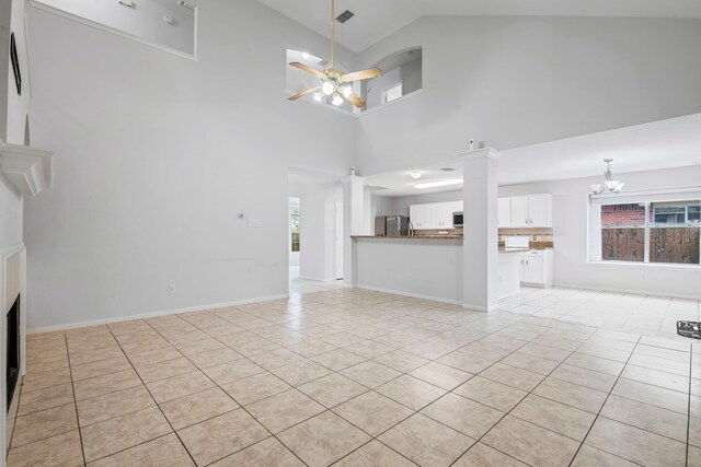 unfurnished living room featuring a fireplace, light tile patterned floors, ceiling fan with notable chandelier, and high vaulted ceiling