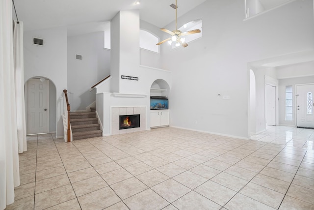 unfurnished living room with ceiling fan, light tile patterned floors, a fireplace, and a high ceiling