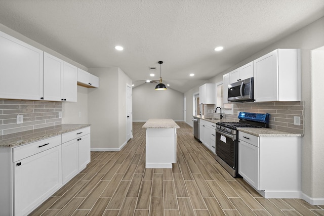 kitchen with appliances with stainless steel finishes, white cabinetry, a kitchen island, and pendant lighting