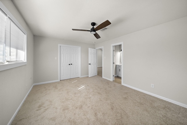 unfurnished bedroom featuring ceiling fan, light colored carpet, and ensuite bath