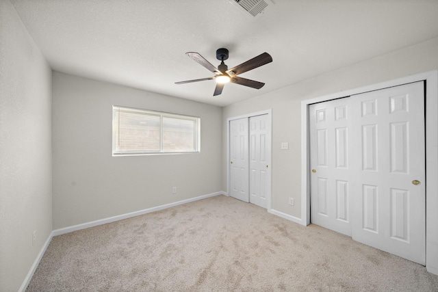 unfurnished bedroom with ceiling fan, light carpet, and multiple closets