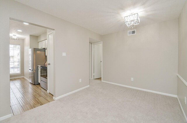 unfurnished room with light colored carpet and a notable chandelier