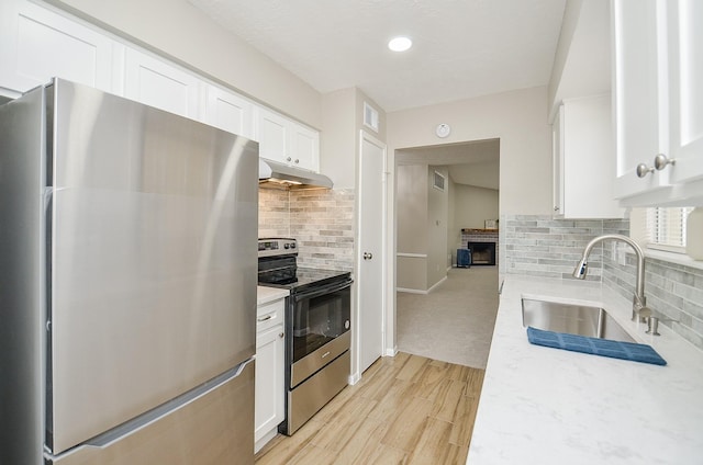 kitchen featuring sink, appliances with stainless steel finishes, white cabinetry, a fireplace, and decorative backsplash