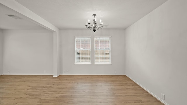 spare room featuring light hardwood / wood-style floors and a notable chandelier