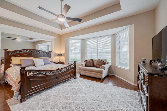 bedroom featuring ceiling fan, a tray ceiling, and light wood-type flooring