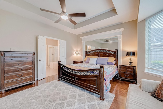 bedroom featuring ceiling fan, hardwood / wood-style floors, a raised ceiling, and multiple windows