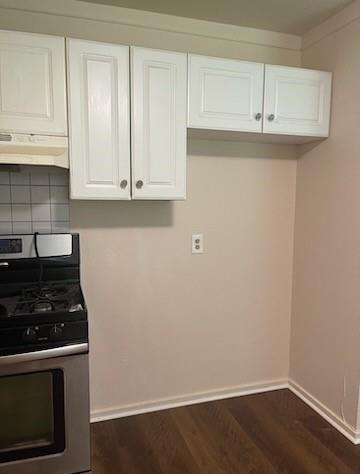 8130 Rockford Dr, Houston, TX 77033 - kitchen featuring stainless steel range with gas cooktop, under cabinet range hood, baseboards, white cabinets, and dark wood finished floors