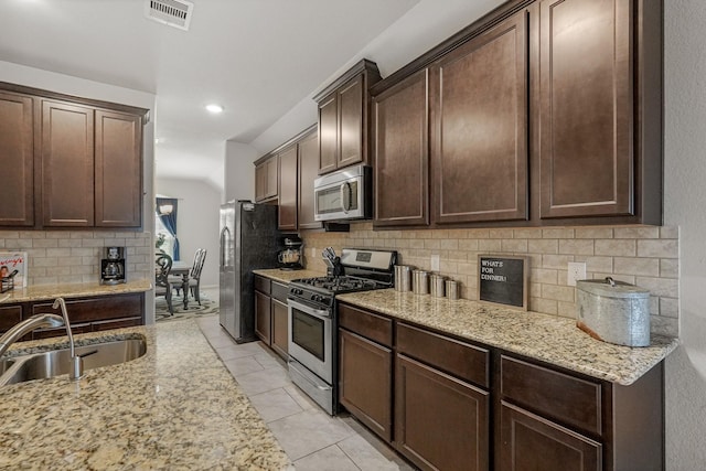 kitchen featuring sink, appliances with stainless steel finishes, dark brown cabinets, light tile patterned flooring, and light stone counters