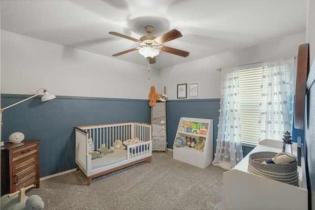 carpeted bedroom featuring ceiling fan and a nursery area