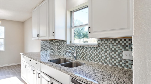 kitchen featuring backsplash, white cabinetry, sink, and light stone counters