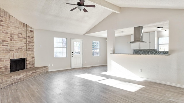 unfurnished living room featuring light wood-type flooring, a textured ceiling, ceiling fan, lofted ceiling with beams, and a fireplace