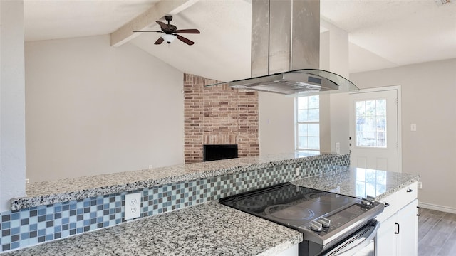 kitchen featuring stove, decorative backsplash, light stone counters, white cabinetry, and island exhaust hood