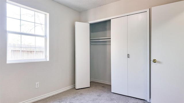 unfurnished bedroom featuring multiple windows, light carpet, a closet, and a textured ceiling