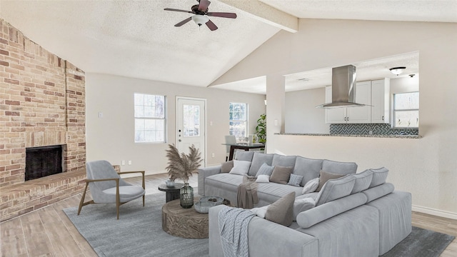 living room with hardwood / wood-style flooring, vaulted ceiling with beams, a textured ceiling, and a brick fireplace