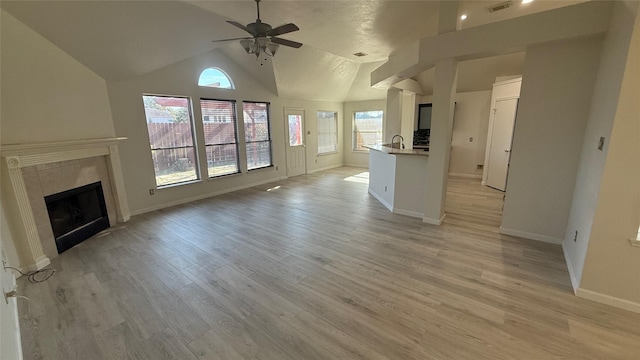 unfurnished living room featuring ceiling fan, vaulted ceiling, a tile fireplace, and light hardwood / wood-style flooring