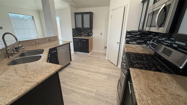 kitchen featuring backsplash, sink, light wood-type flooring, light stone counters, and stainless steel appliances