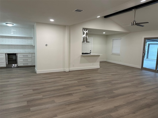 unfurnished living room featuring wine cooler, ceiling fan, dark hardwood / wood-style flooring, and lofted ceiling with beams