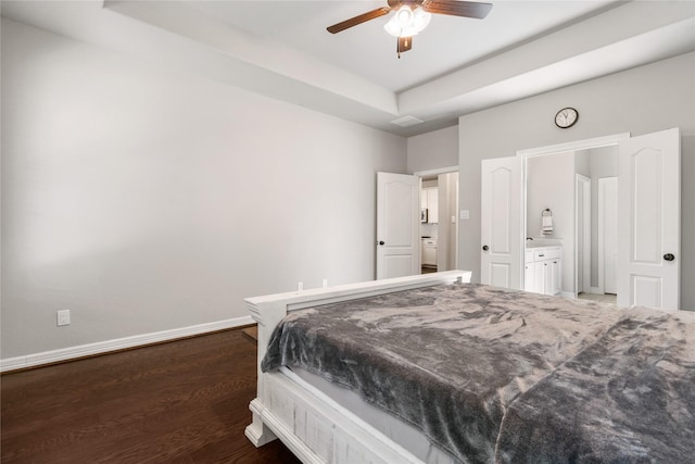 bedroom featuring ceiling fan, ensuite bath, dark hardwood / wood-style flooring, and a tray ceiling