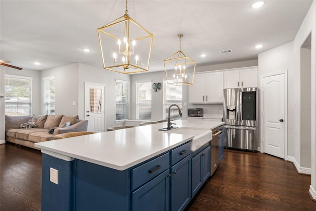 kitchen with stainless steel fridge, blue cabinetry, white cabinetry, a center island with sink, and decorative light fixtures