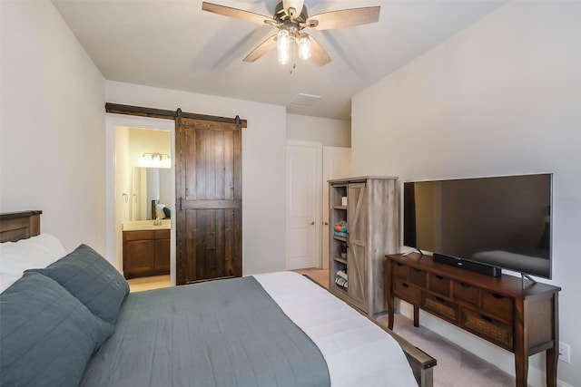 bedroom with a barn door, light colored carpet, ceiling fan, and connected bathroom