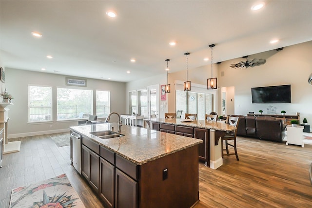 kitchen featuring a center island with sink, light stone counters, hanging light fixtures, and sink