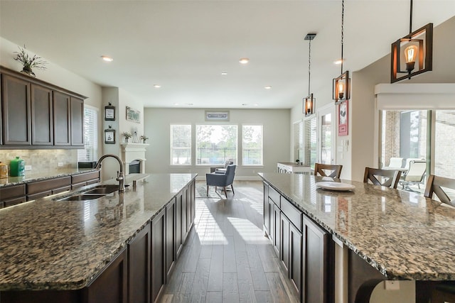 kitchen with dark brown cabinetry, light stone counters, a large island, and sink