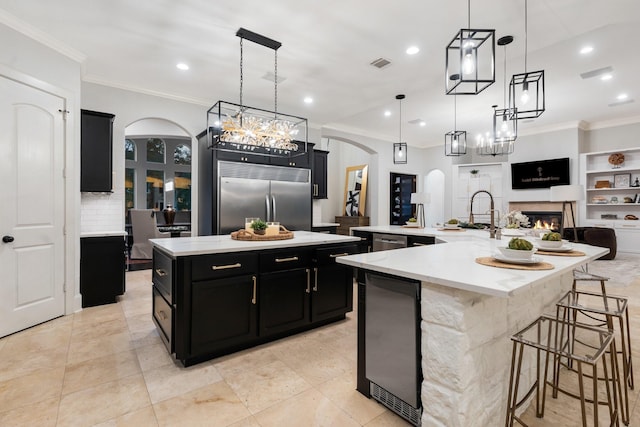 kitchen with built in fridge, built in shelves, hanging light fixtures, and a large island with sink