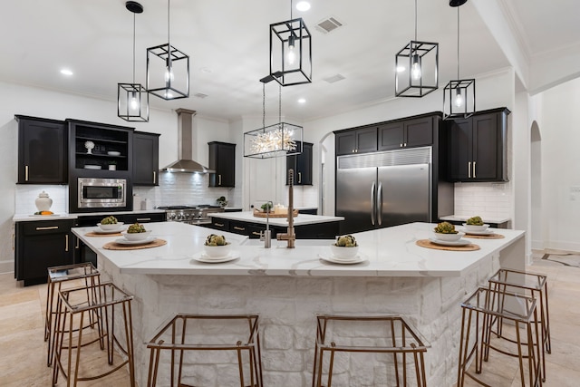 kitchen featuring hanging light fixtures, built in appliances, wall chimney exhaust hood, and a large island