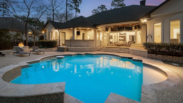 pool at dusk with ceiling fan, a patio area, and an outdoor living space with a fire pit