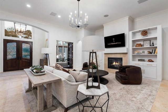 living room featuring a tile fireplace, french doors, an inviting chandelier, and crown molding