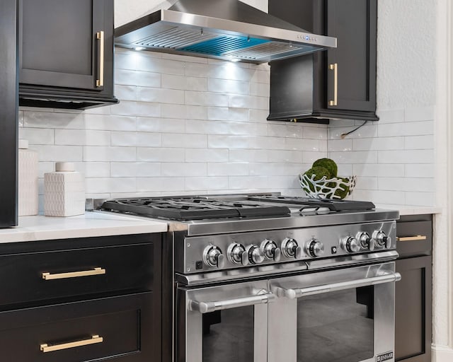 kitchen featuring decorative backsplash, range with two ovens, and wall chimney range hood