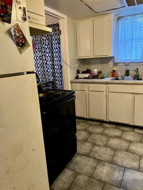 kitchen with a textured ceiling, sink, white fridge, white cabinetry, and black / electric stove