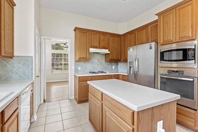 kitchen with light tile patterned floors, tasteful backsplash, appliances with stainless steel finishes, light countertops, and under cabinet range hood