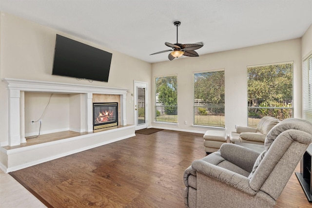 living room with dark wood-style floors, baseboards, a ceiling fan, and a glass covered fireplace