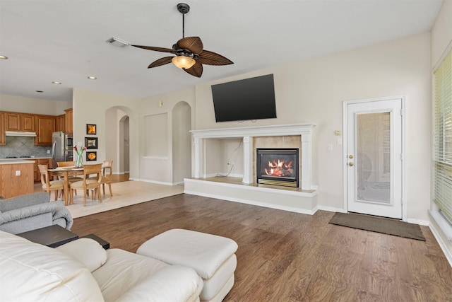 living room featuring baseboards, visible vents, arched walkways, wood finished floors, and a fireplace