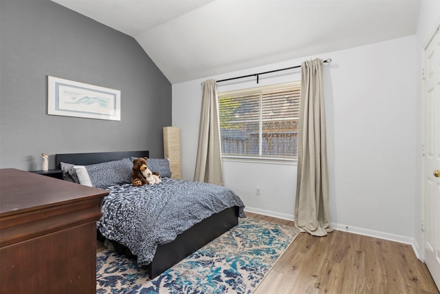 bedroom with vaulted ceiling, wood finished floors, and baseboards