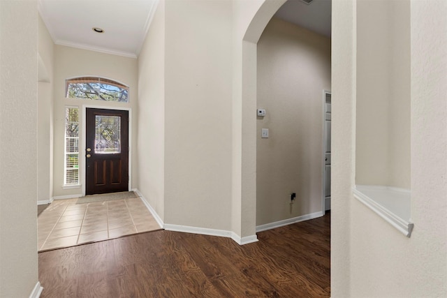 foyer featuring baseboards, arched walkways, wood finished floors, and ornamental molding