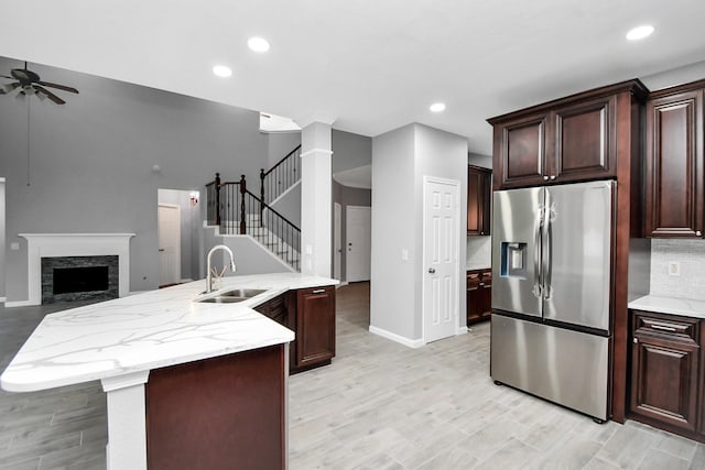 kitchen with stainless steel fridge, ceiling fan, a kitchen island with sink, sink, and a stone fireplace