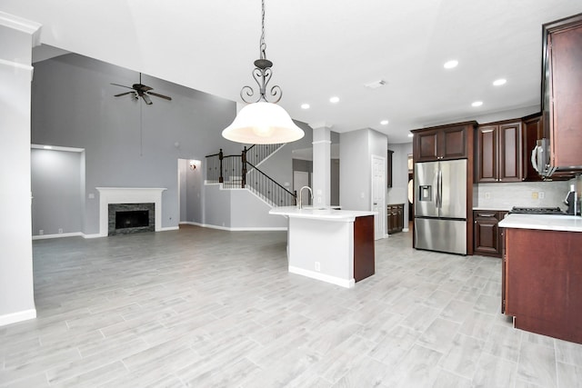 kitchen with a kitchen island with sink, a stone fireplace, hanging light fixtures, ceiling fan, and appliances with stainless steel finishes