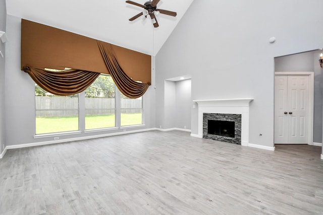 unfurnished living room with ceiling fan, a stone fireplace, light wood-type flooring, and high vaulted ceiling