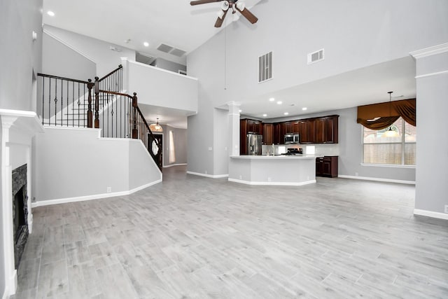 unfurnished living room featuring a towering ceiling, light hardwood / wood-style flooring, and ceiling fan