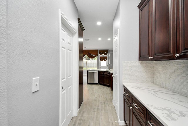 kitchen featuring decorative backsplash, light stone counters, stainless steel dishwasher, sink, and light hardwood / wood-style floors